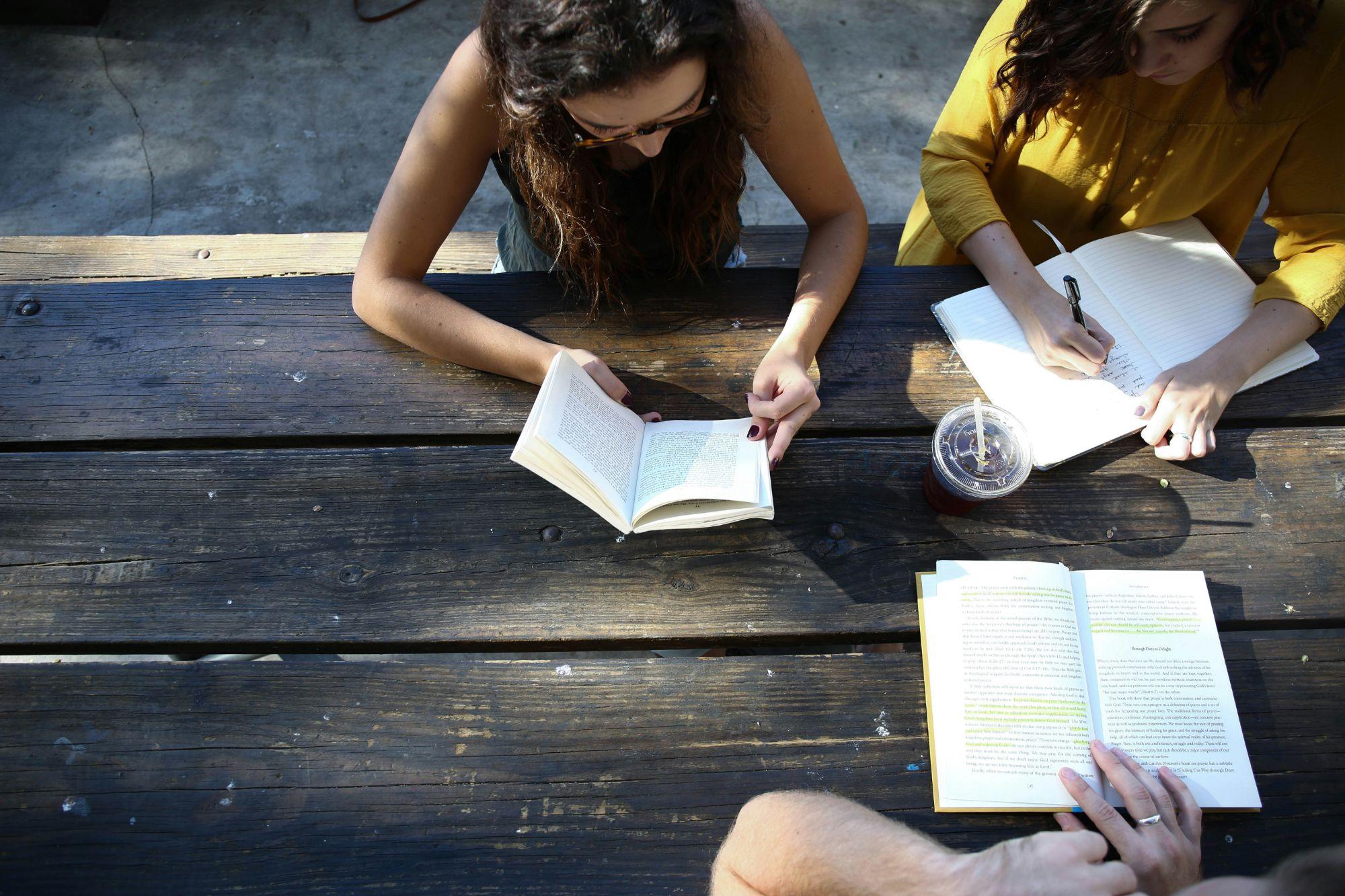 Writers reading and writing together at a sunlit wooden table
